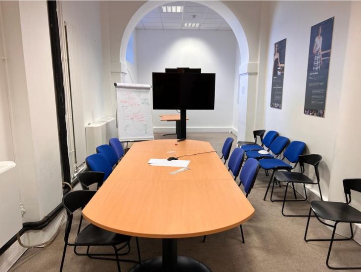 Salle de réunion vide avec des chaises disposées autour d'une grande table et un écran de présentation.